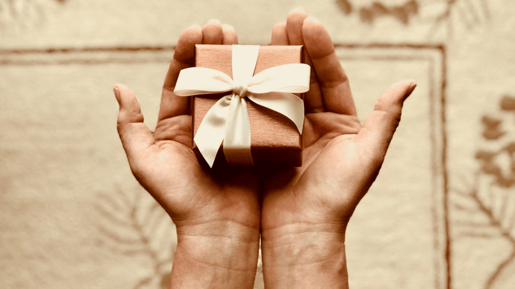 Two hands holding a small gift wrapped with a ribbon.